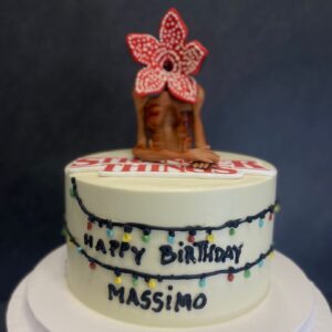 Torta personalizzata a tema serie tv con luci decorative colorate e topper a forma di creatura fantastica con fiore rosso, scritta "Happy Birthday Massimo" - Piece of Cake Italia